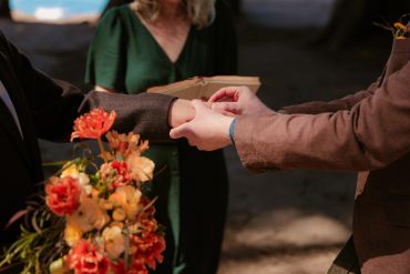 Two people holding hands during a ceremony with flowers.