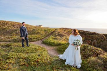Bride and groom standing on grassy cliffs with an ocean view.