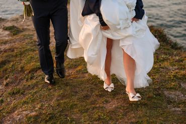 Bride and groom walking on grass near water.