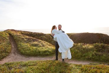 Groom carries bride on a scenic outdoor path during sunset.