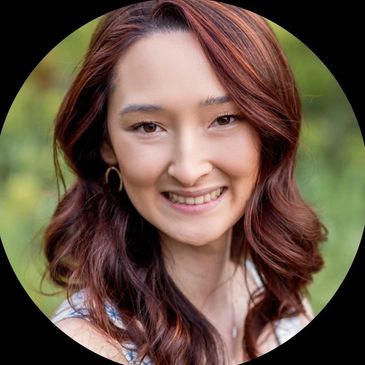 Smiling woman with wavy auburn hair outdoors.