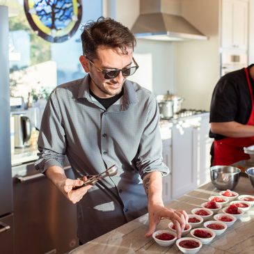 Man in sunglasses preparing multiple bowls of food in a kitchen.