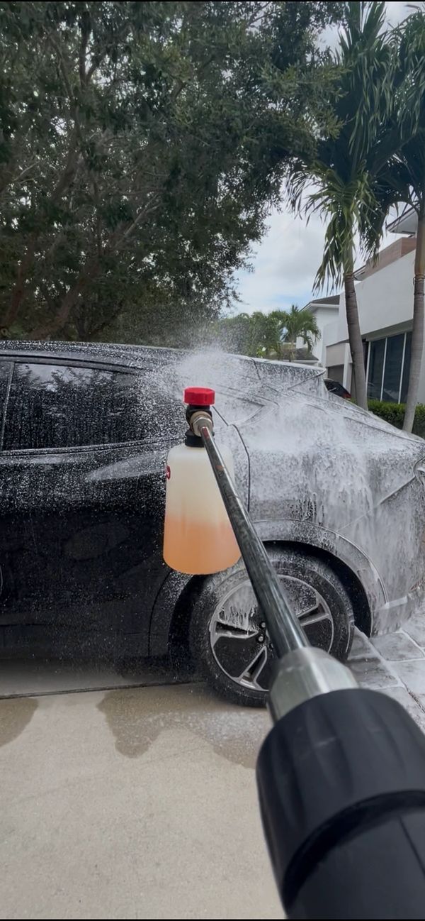 Foam being sprayed on a black car using a pressure washer with a foam cannon.