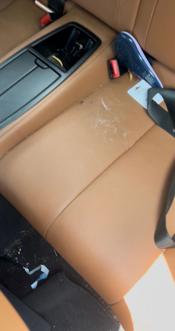Car back seat with tan leather and some debris including a shoe and a tag.