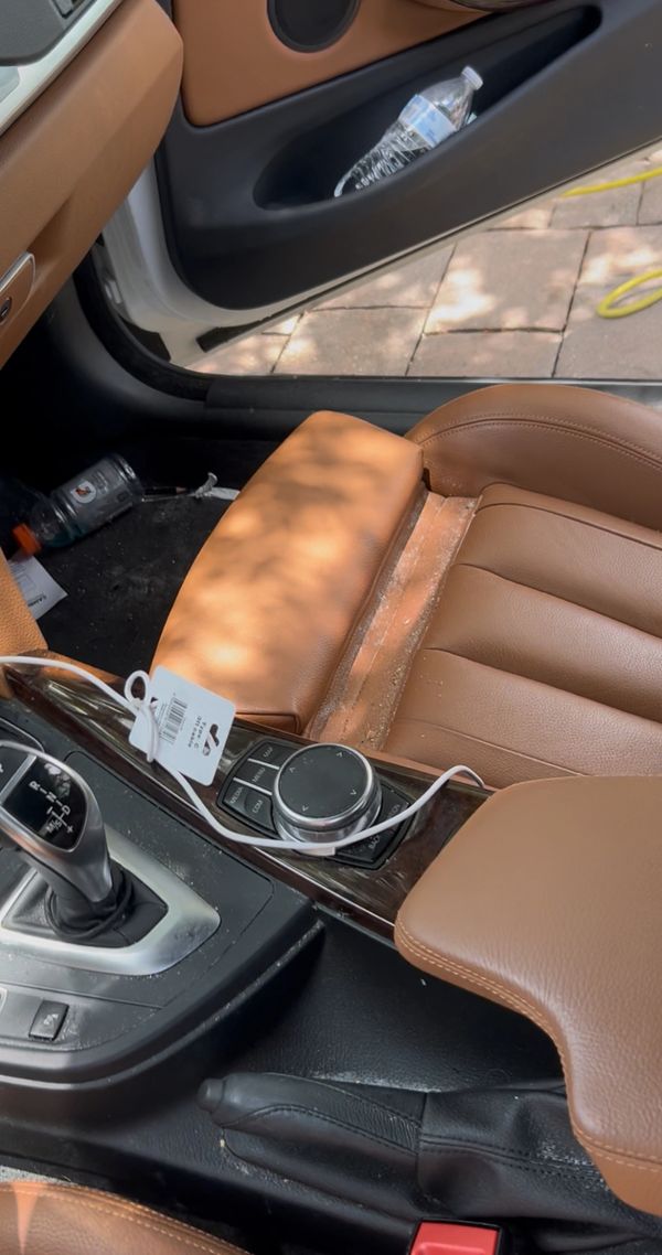Car interior with brown leather seats and gear shift, showing some clutter and a charging cable.