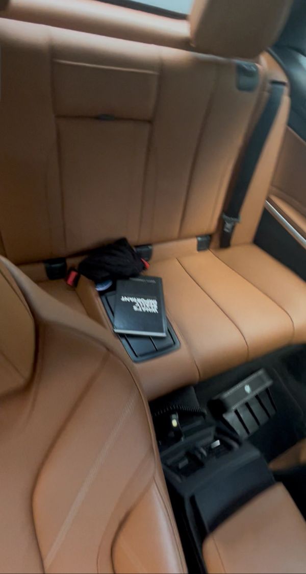 Luxury tan leather car interior with a book and black cloth on the back seat.