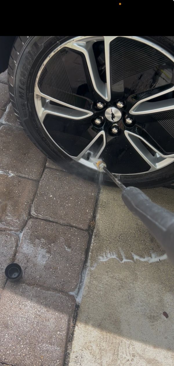 Cleaning a car wheel with a pressure washer on a paved surface.