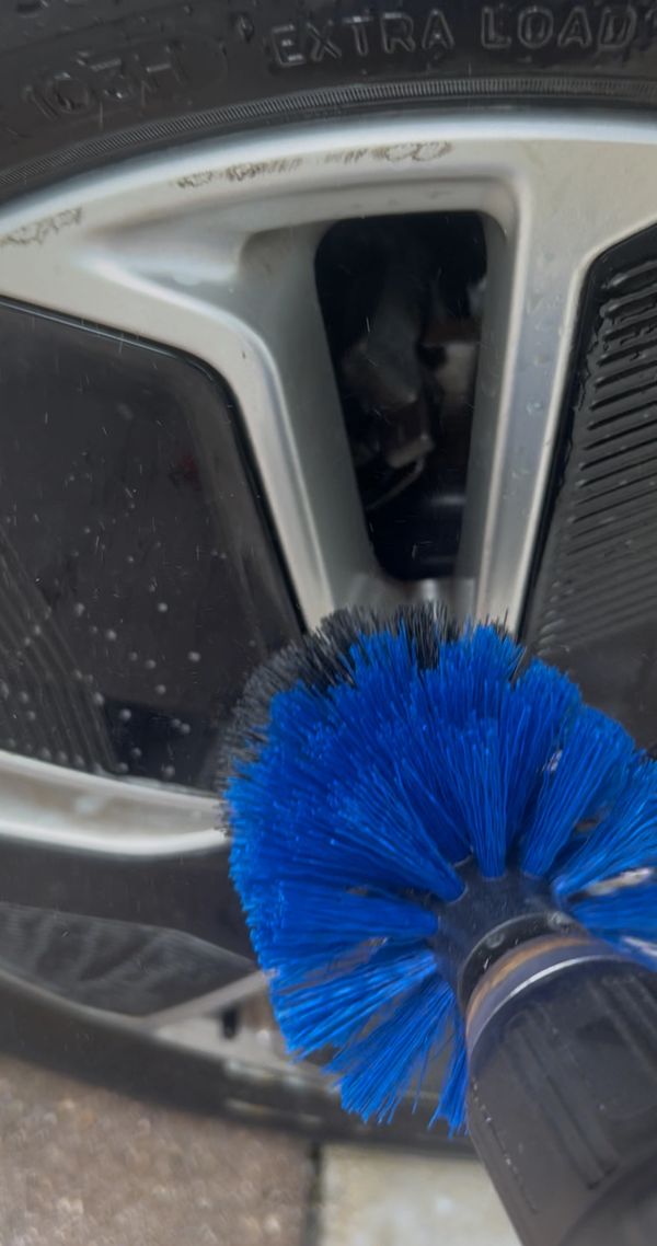 Blue brush cleaning a car wheel rim.