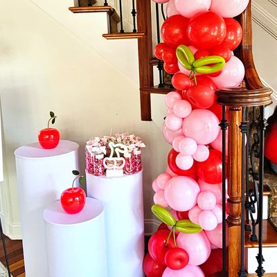 Red and pink balloon garland with cherries installed on a staircase railing.