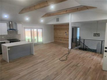 Modern open-concept kitchen and living area with wood flooring and exposed beams.