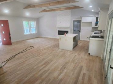 Spacious modern kitchen and living area with light wood floors and exposed ceiling beams.
