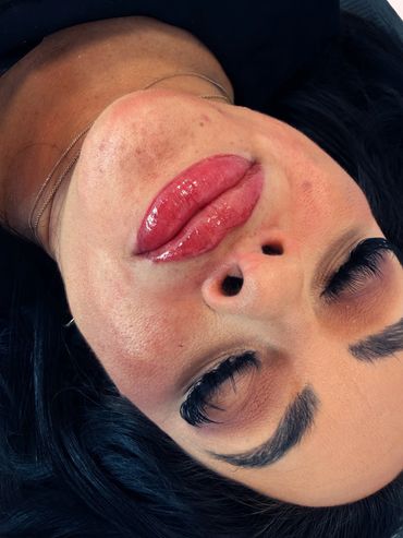 Close-up of a woman's face with glossy lips and long eyelashes, eyes closed.