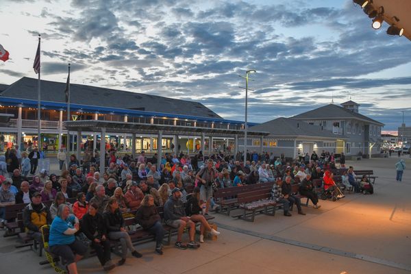 Large crowd sitting outdoors during dusk at a building complex.