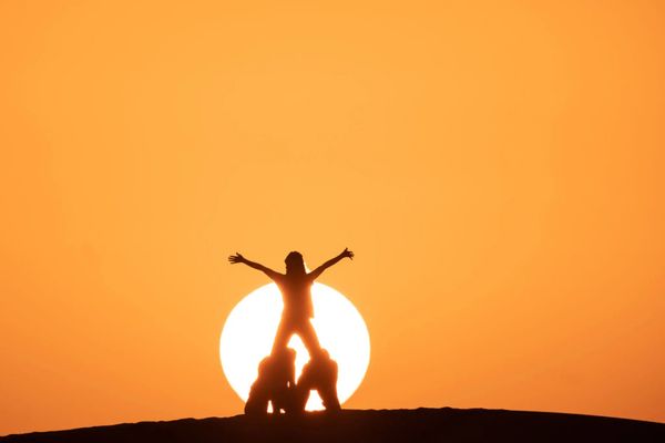 A woman standing on top of her head in front of the sun.