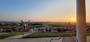 Crowd enjoying a sunset event at an outdoor venue with a winged horse statue.