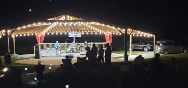 Outdoor nighttime band performance under string lights with audience silhouettes.