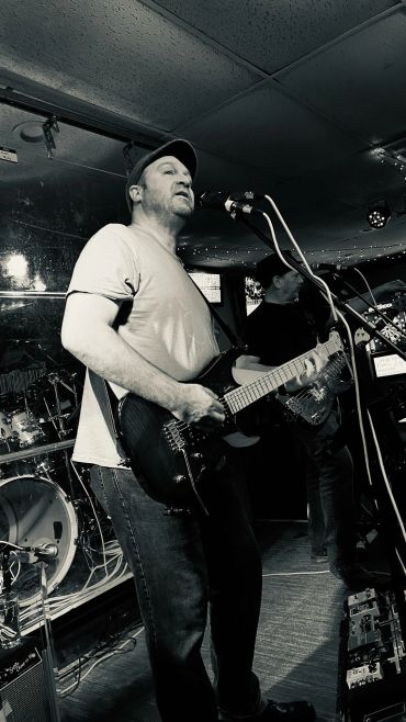 Musician passionately playing electric guitar and singing on stage in a dimly lit venue.