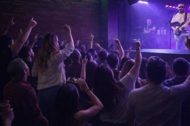 Crowd enjoying a live music concert with raised hands and stage lighting.