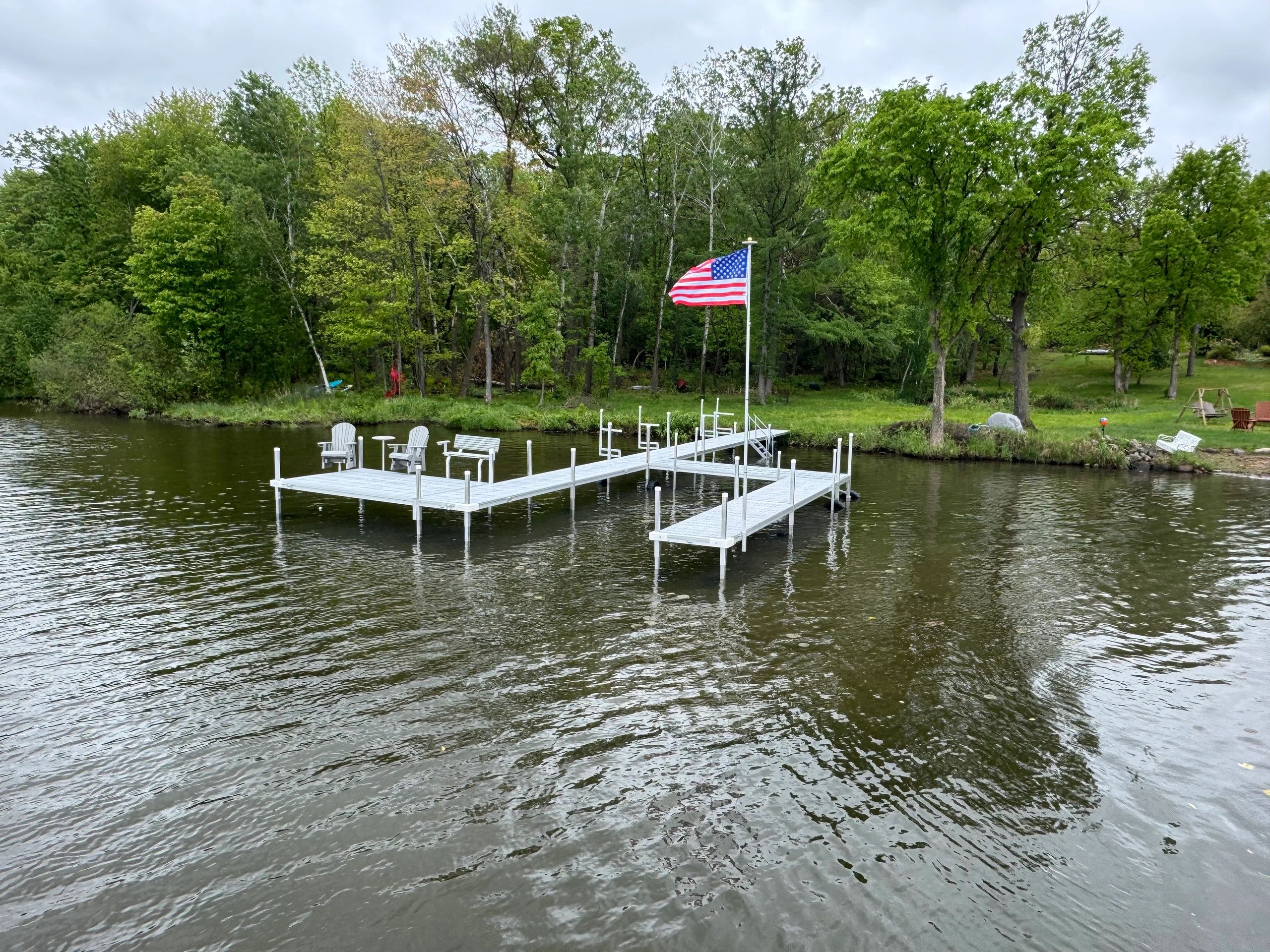 A wooden dock with chairs and an American flag on a lake.