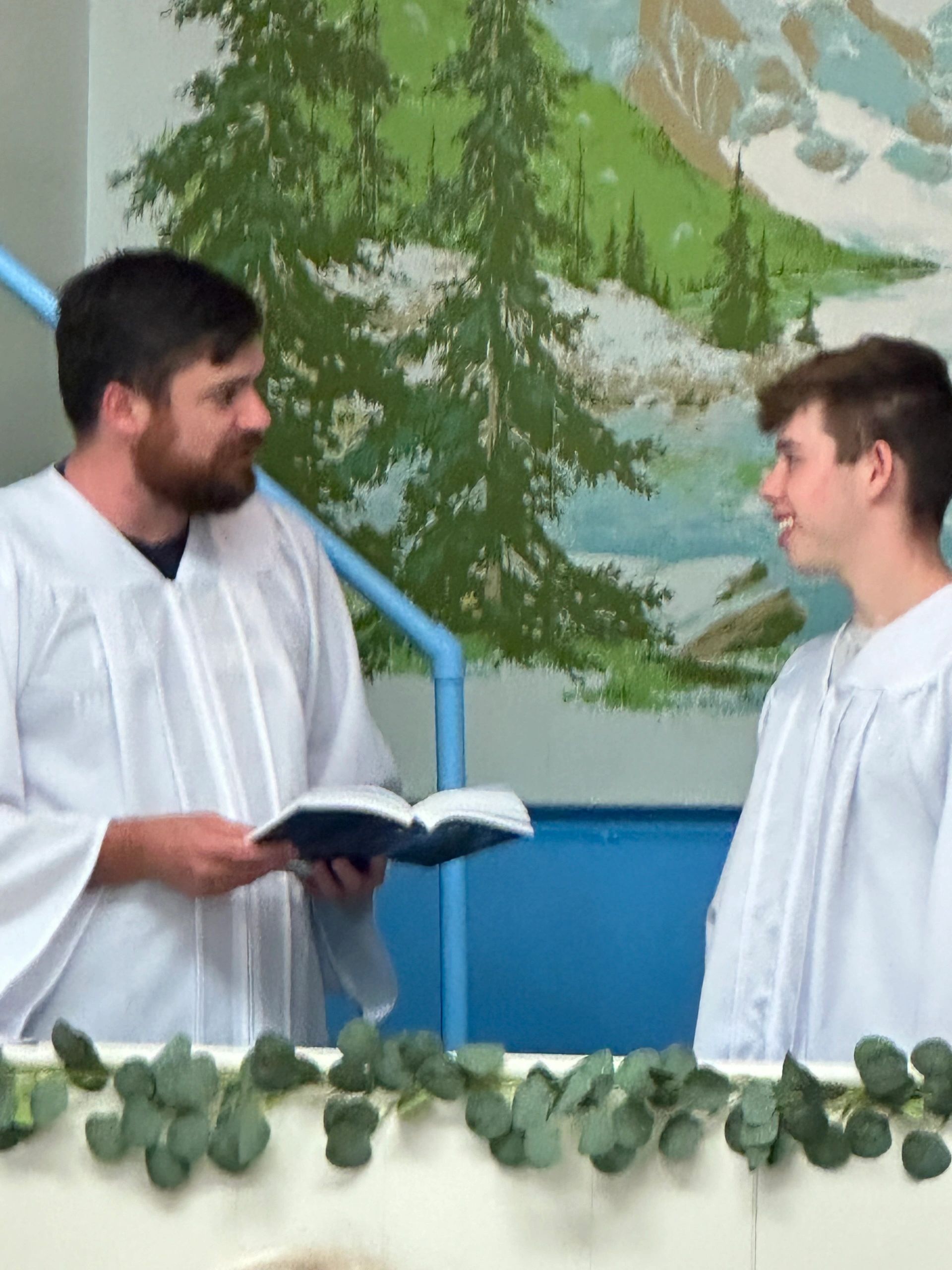 Two men in white robes engage in conversation with a book between them.