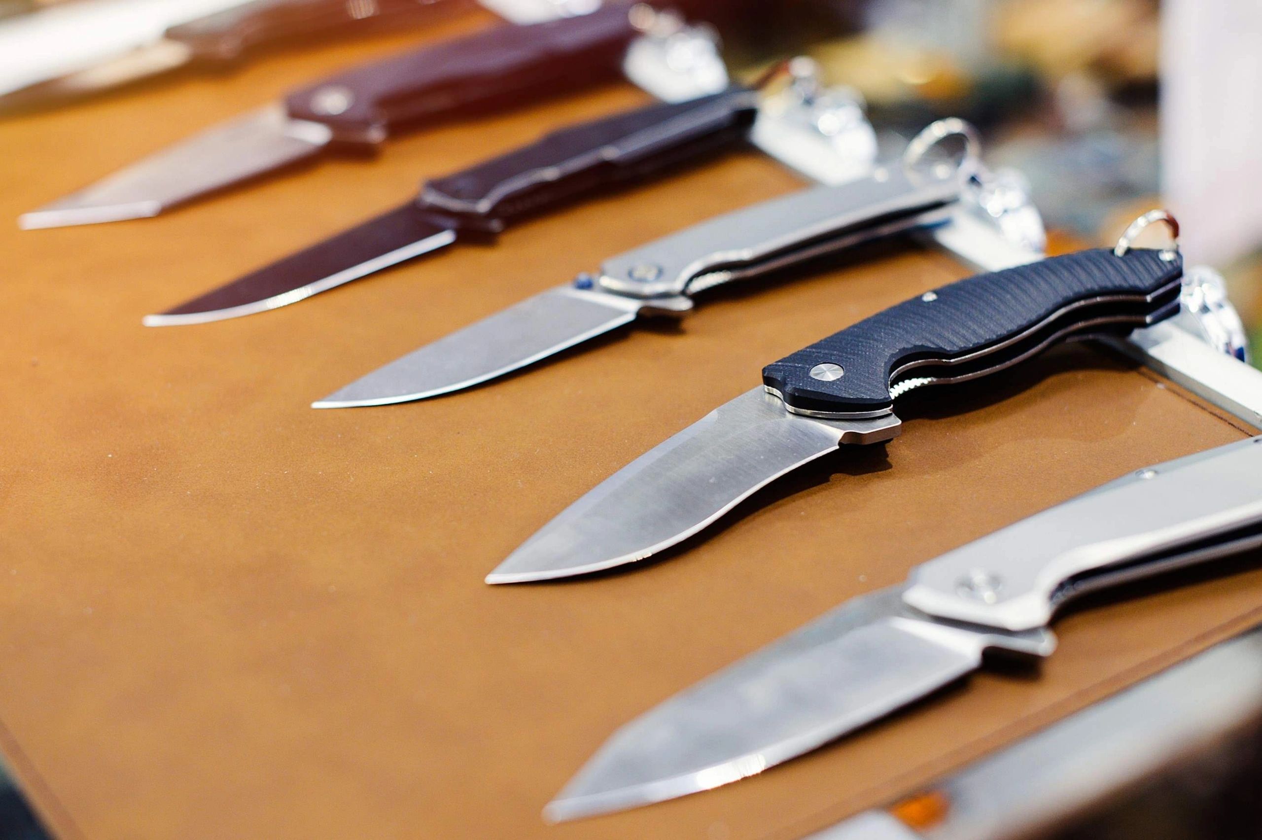 A row of folding knives displayed on a brown surface.