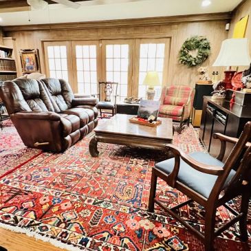 Cozy living room with leather sofa, wooden chairs, and vibrant Persian rug.
