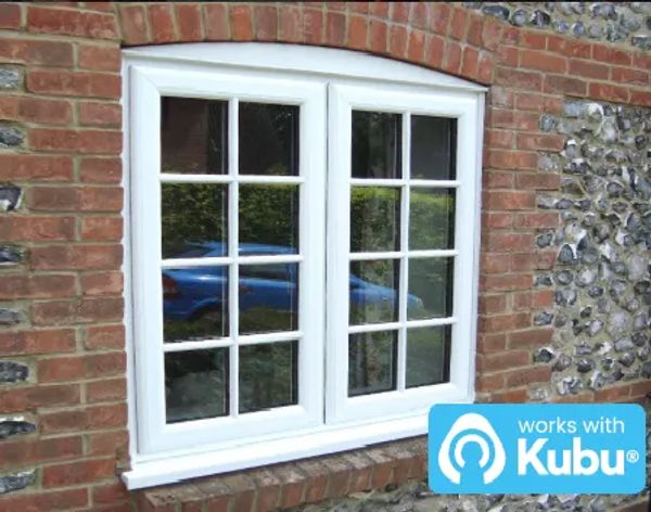 White framed window with grid panes on a brick and flint wall.