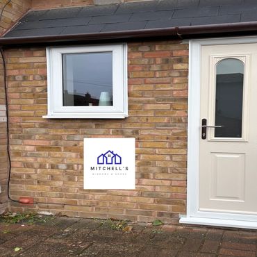 White door and window installed on brick wall with Mitchell's Windows & Doors logo.