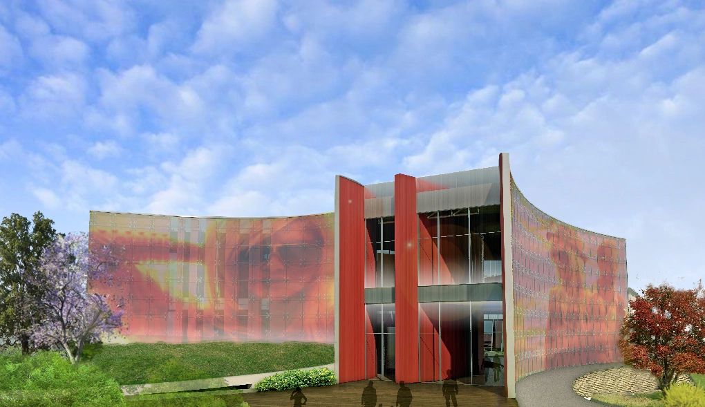 Edificio moderno con tonalità rosse e arancioni, immerso in un paesaggio verde sotto un cielo blu.