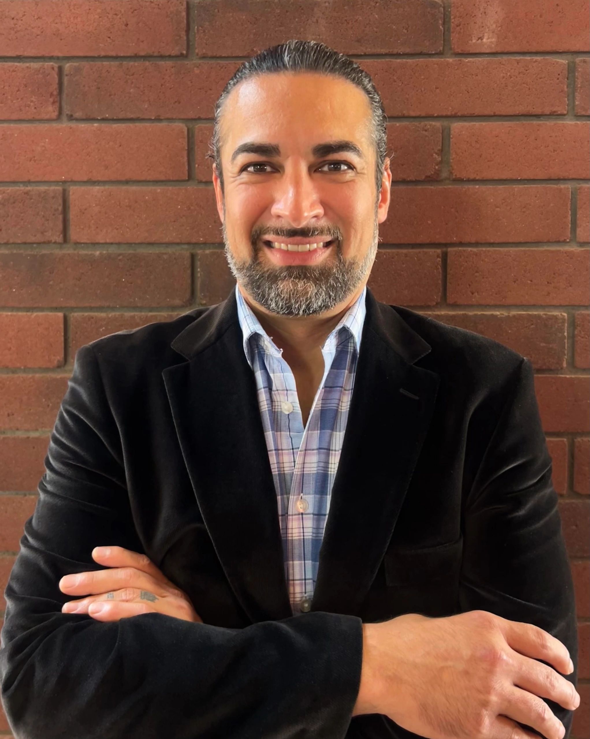 Man with beard smiling confidently in front of a brick wall.