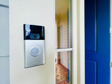 A Ring video doorbell installed next to a blue front door with a glass panel.