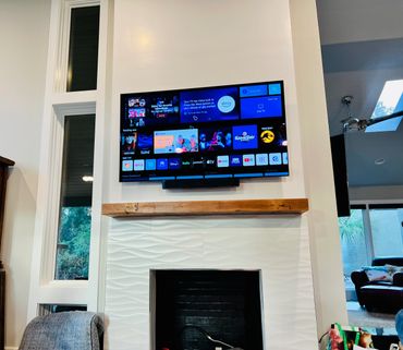 Modern living room with wall-mounted TV above a fireplace and decorative wooden mantel.