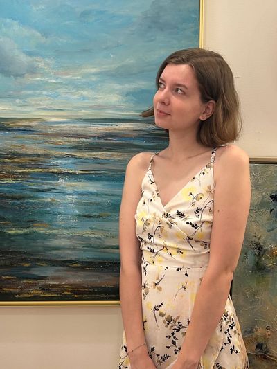 Young woman in floral dress posing thoughtfully by a seascape painting.