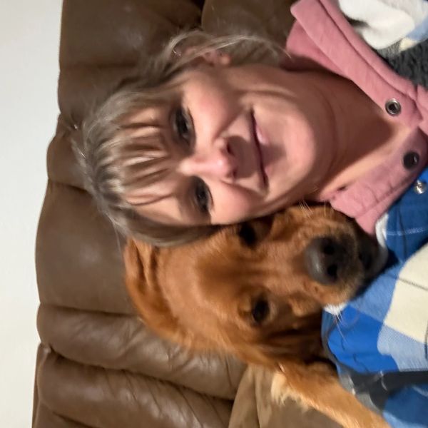 Woman smiling with her golden retriever on a couch.