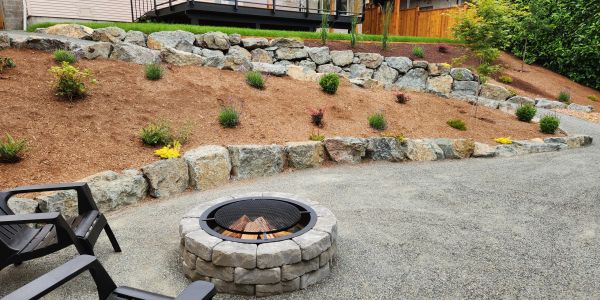 A backyard fire pit with chairs and a landscaped garden with rocks and plants.