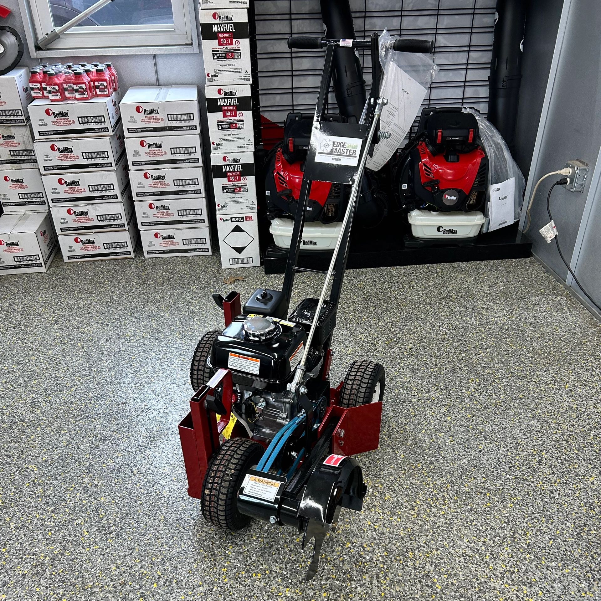 A heavy-duty garden tiller with RedMax fuel and oil products in the background.