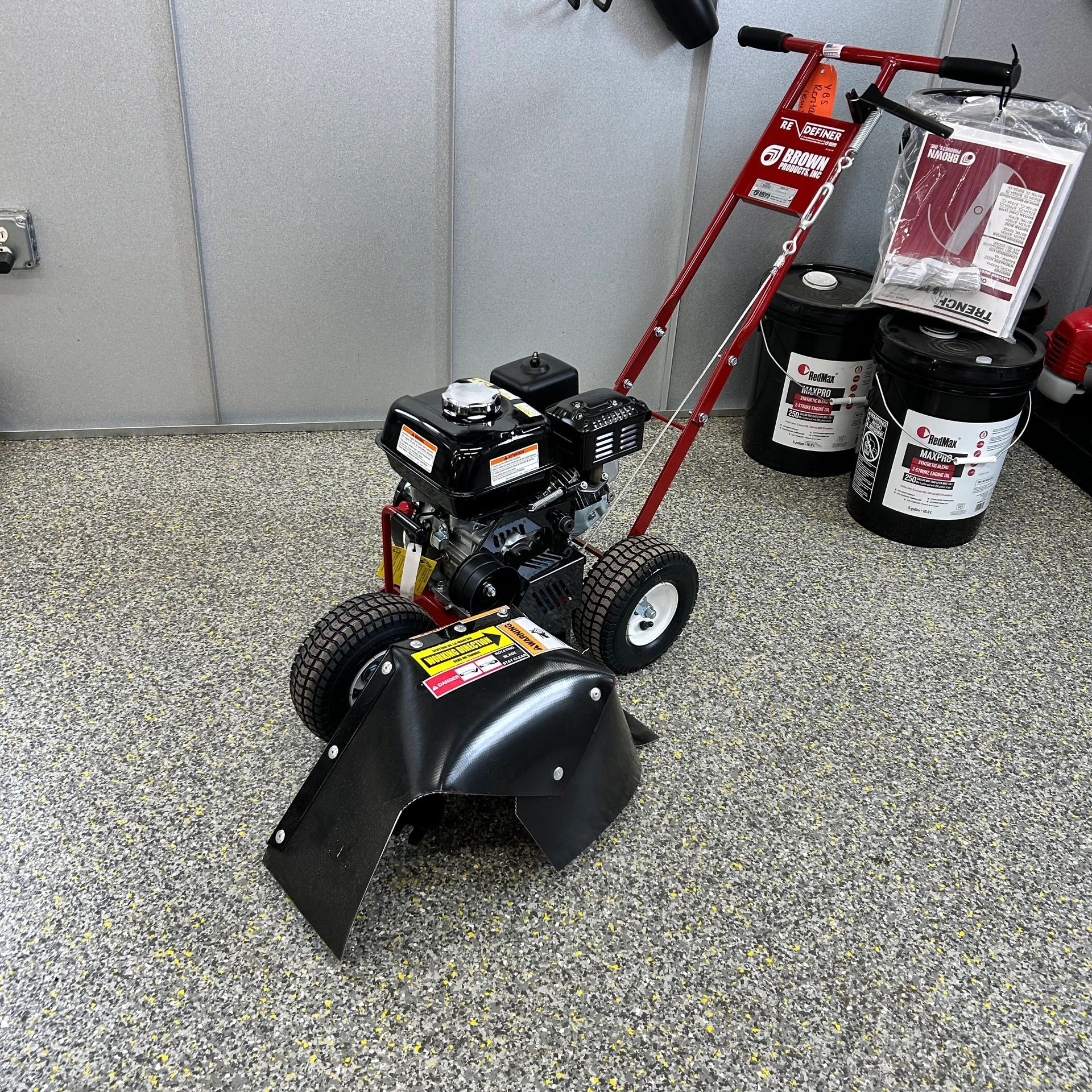 A red and black garden tiller with engine oil buckets in the background.