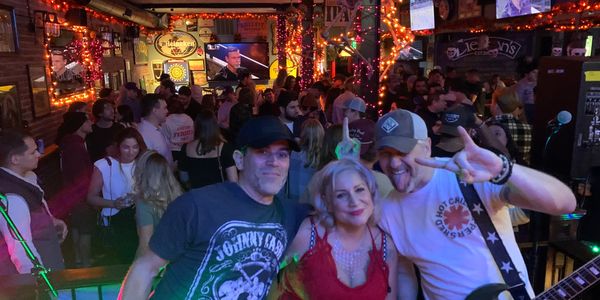 A lively bar scene with a crowd and three friends posing joyfully in the foreground.