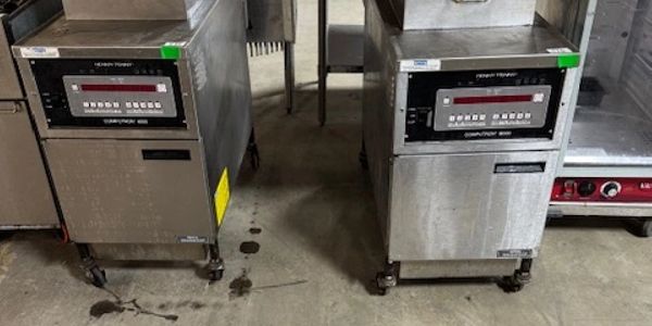Two stainless steel Henny Penny commercial fryers on wheels in a kitchen.