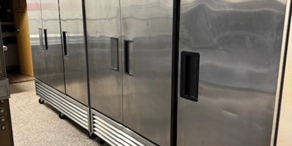 Row of large stainless steel commercial refrigerators in a kitchen.
