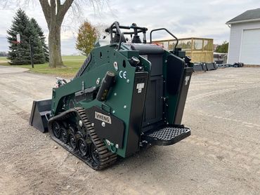 Compact green tracked skid steer loader parked on gravel.