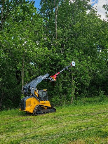 Yellow robotic forestry machine with an extended arm cutting trees.