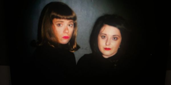 Two women with serious expressions in dark clothing.