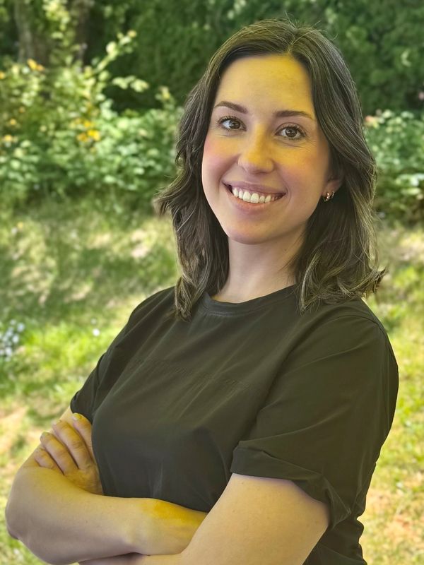 Smiling woman with folded arms standing outdoors in a garden.