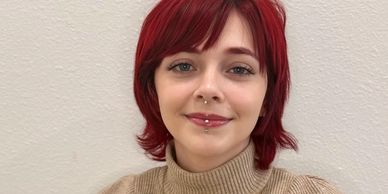 Smiling young woman with red hair and piercings.