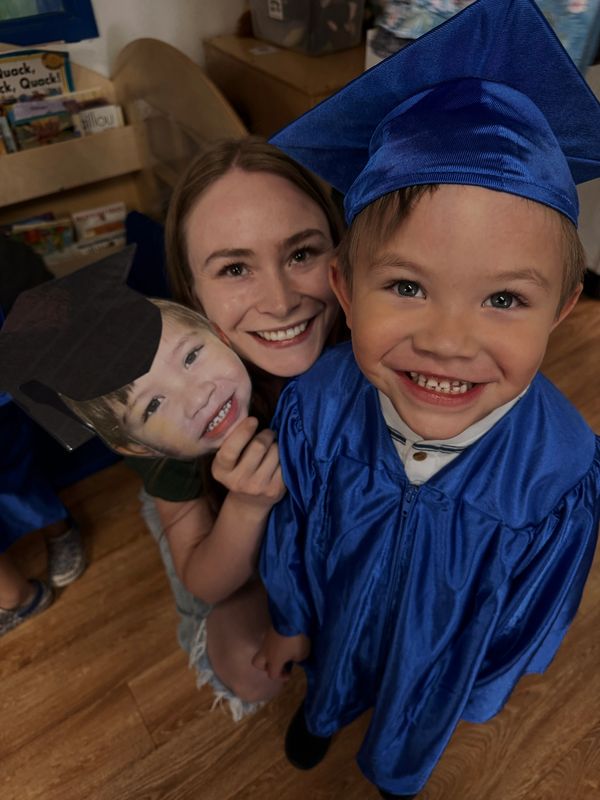 Smiling child in blue graduation gown and cap, woman holding a cutout of child's face.
