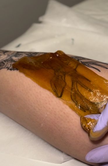 A person removing a wax strip from a tattooed arm.