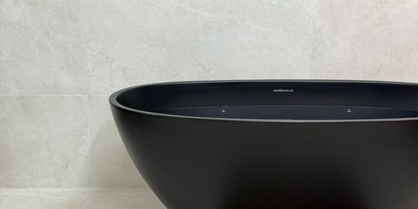 Modern black freestanding bathtub against a light tiled wall.