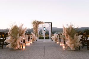 Elegant outdoor wedding aisle adorned with pampas grass and candles at sunset.