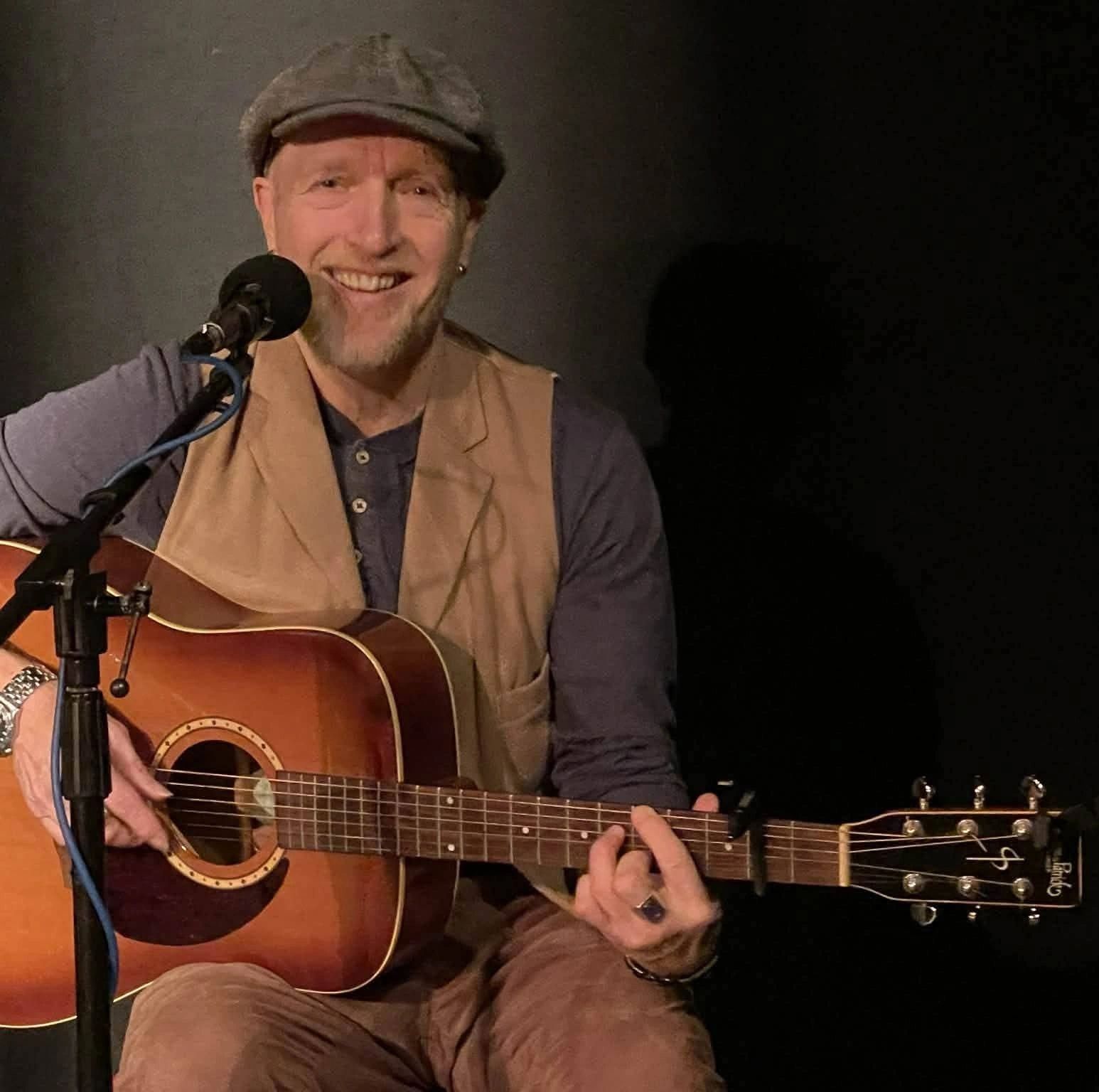 Smiling man playing acoustic guitar and singing into a microphone.